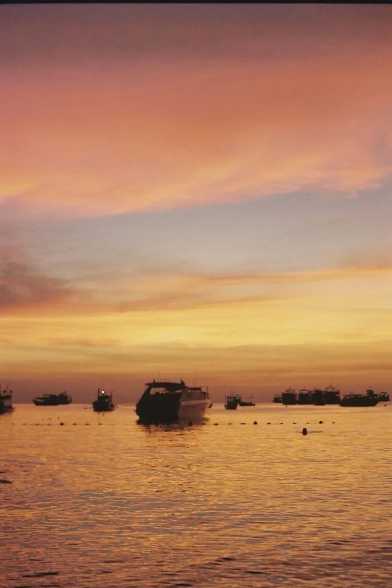 Boats on calm water under a pink and gold sunset